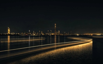 Cinematic nighttime city skyline with gold light trails reflected across the waterfront